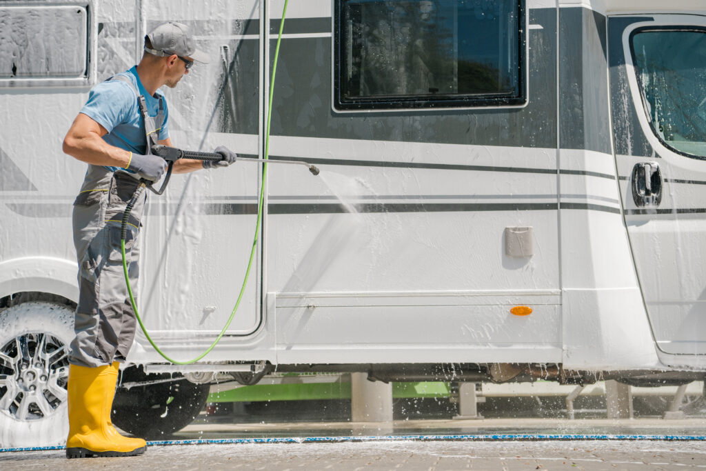 Man pressure washing RV exterior at home or service site
